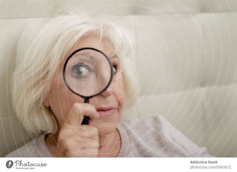 Ältere Frau mit Vergrößerungsglas Rentnerin neugierig positiv Bett Schlafzimmer Komfort Lupe Interesse warme Kleidung heimwärts Senior blond im Inneren
