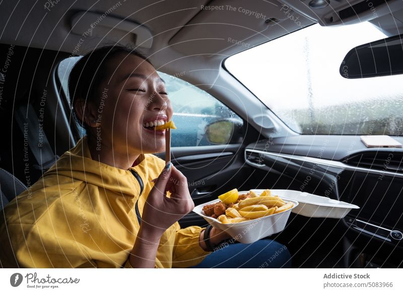Asiatische Frau isst Chips im Auto essen gebraten Kartoffel PKW hölzern Gabel Snack Fastfood Regen Großbritannien vereinigtes königreich heiter asiatisch
