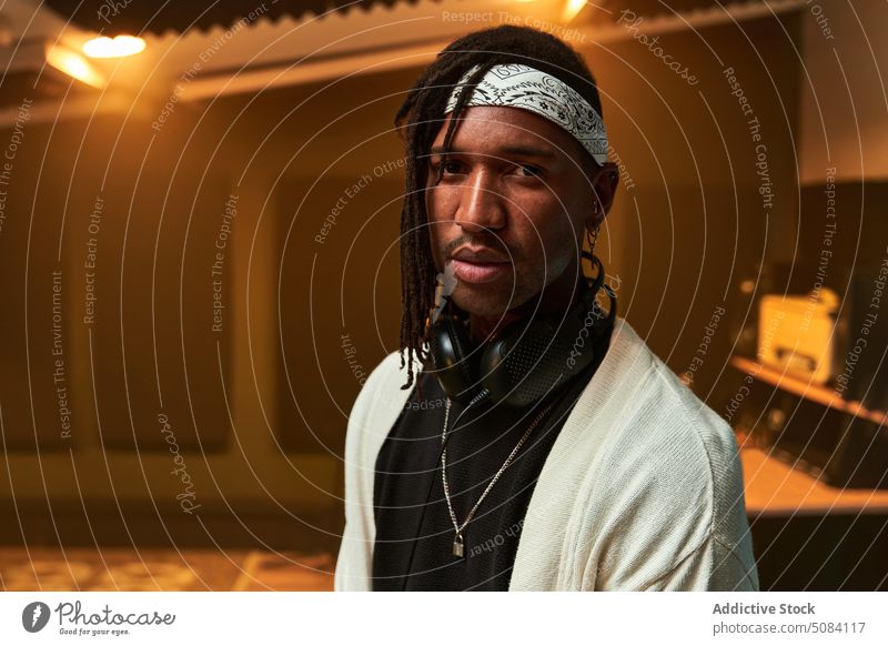 Schwarzer Mann mit Kopfhörern im Nacken sitzt im Studio Porträt Musiker Aufzeichnen Atelier Kälte glühen Licht Vergnügen Persönlichkeit männlich akustisch