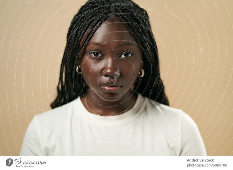 Ruhige schwarze Frau schaut in die Kamera Model Porträt Afro-Zöpfe Vorschein Persönlichkeit Atelier beiger Hintergrund Menschliches Gesicht Windstille Dame jung