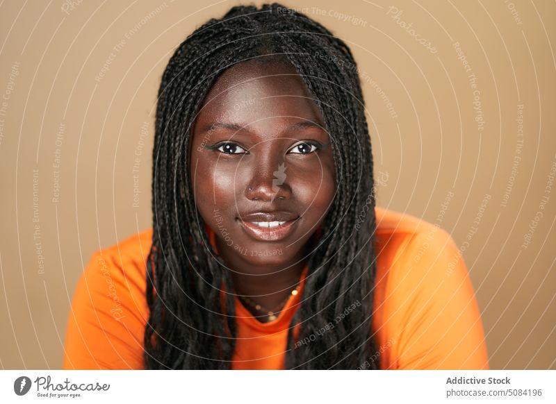 Ruhige glückliche schwarze Frau schaut in die Kamera Model Porträt Lächeln Afro-Zöpfe Vorschein Persönlichkeit Atelier brauner Hintergrund Menschliches Gesicht
