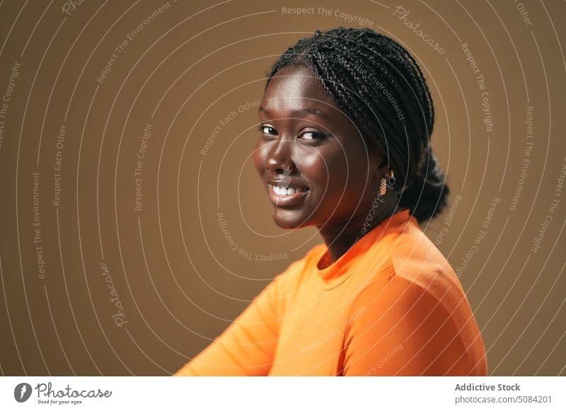 Ruhige glückliche schwarze Frau schaut in die Kamera Model Porträt Lächeln Afro-Zöpfe Vorschein Persönlichkeit Atelier brauner Hintergrund Menschliches Gesicht