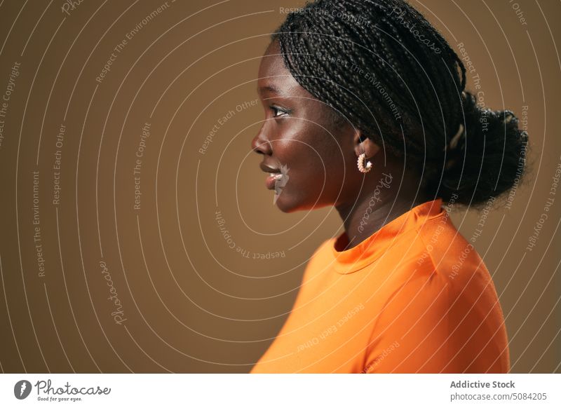Ruhige glückliche schwarze Frau schaut weg Model Porträt Lächeln Afro-Zöpfe Vorschein Persönlichkeit Atelier brauner Hintergrund Menschliches Gesicht Windstille