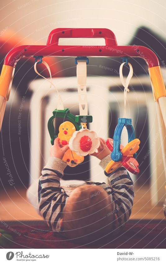 Baby unter einem Spielbogen Kind spielen Motorik motorische Fähigkeiten interessiert neugierig erkunden greifen Hände beobachten Spielzeug Tastsinn jung