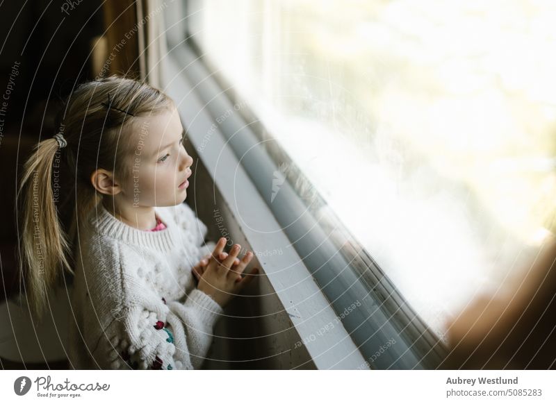 kleines Mädchen mit Zöpfen und Winterpulli schaut aus dem Fenster Weihnachtsmann Hintergrund blond hell Feier Kind Kindheit Weihnachten niedlich Dezember