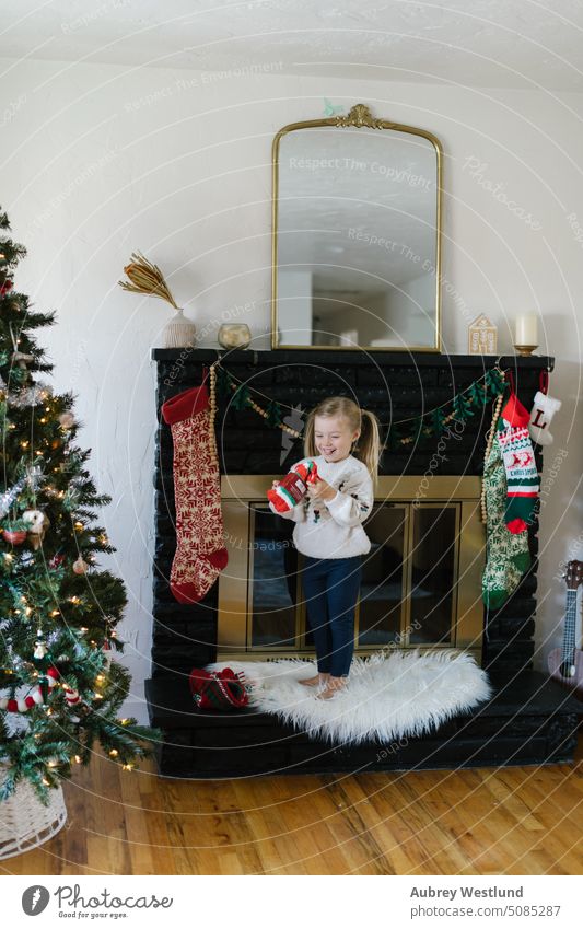 Kleinkind mit blonden Zöpfen und Winterpulli findet Socken in ihrem Weihnachtsstrumpf Weihnachtsmann Hintergrund schwarzer Kamin hell Feier Kind Kindheit