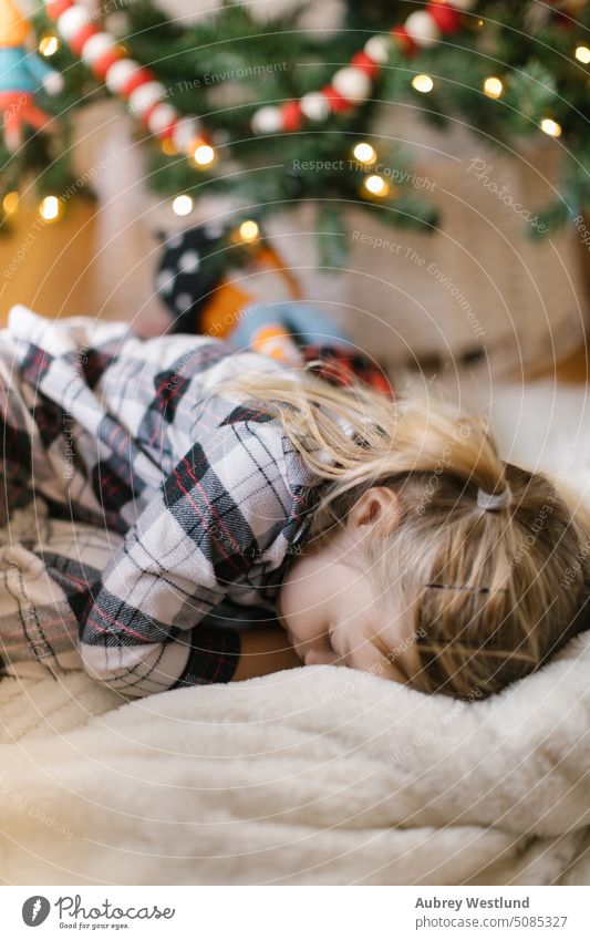 Kleinkind im karierten Pyjama auf einer Decke vor dem Weihnachtsbaum liegend Weihnachtsmann Hintergrund blond hell Feier Kind Kindheit Weihnachten gemütlich