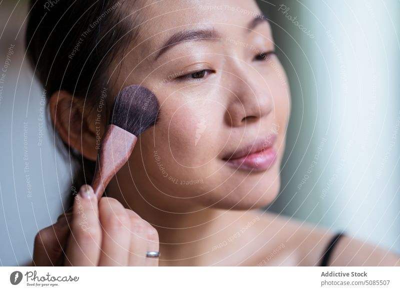 Junge asiatische Frau trägt mit einem Kosmetikpinsel Grundierung auf das Gesicht auf Bürste Fundament Aufstrich Pulver erröten Make-up Schönheit