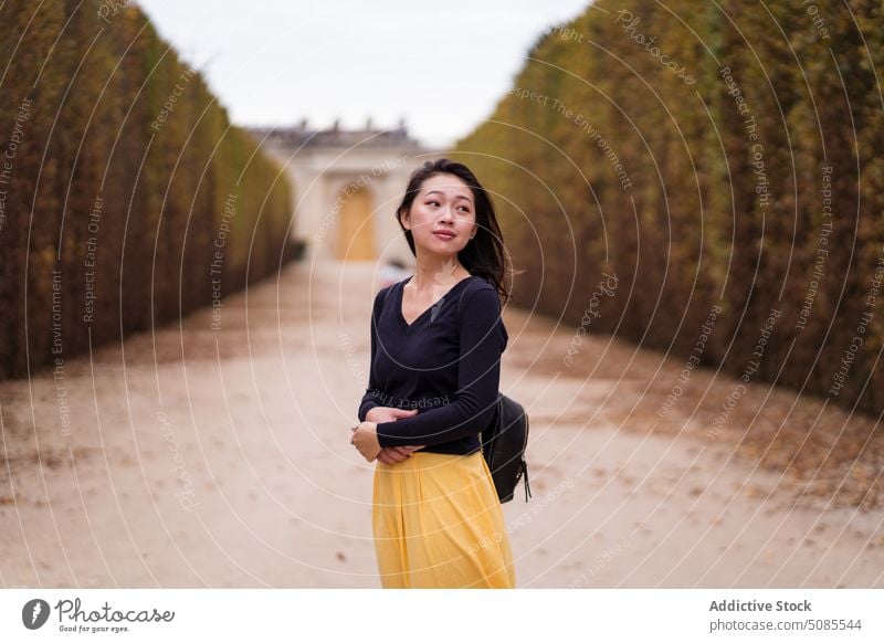 Junge asiatische Frau steht zwischen Gras Zaun Weg Park Gebäude Vorschein Windstille Örtlichkeit Sightseeing Herbst friedlich nachdenklich nachdenken Dame