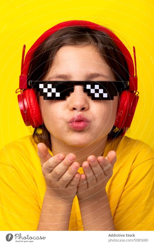Nettes Mädchen sendet Luftkuss, während sie auf gelbem Hintergrund steht Kind senden gestikulieren Kopfhörer Musik Bildpunkt Brille Liebe niedlich bezaubernd