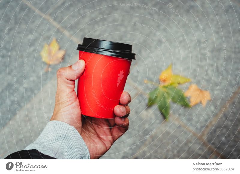 Hand eines Mannes hält einen roten Pappbecher Kaffee und Herbstblätter auf dem Hintergrund Getränk vereinzelt Nahaufnahme Cappuccino Tasse trinken Heißgetränk