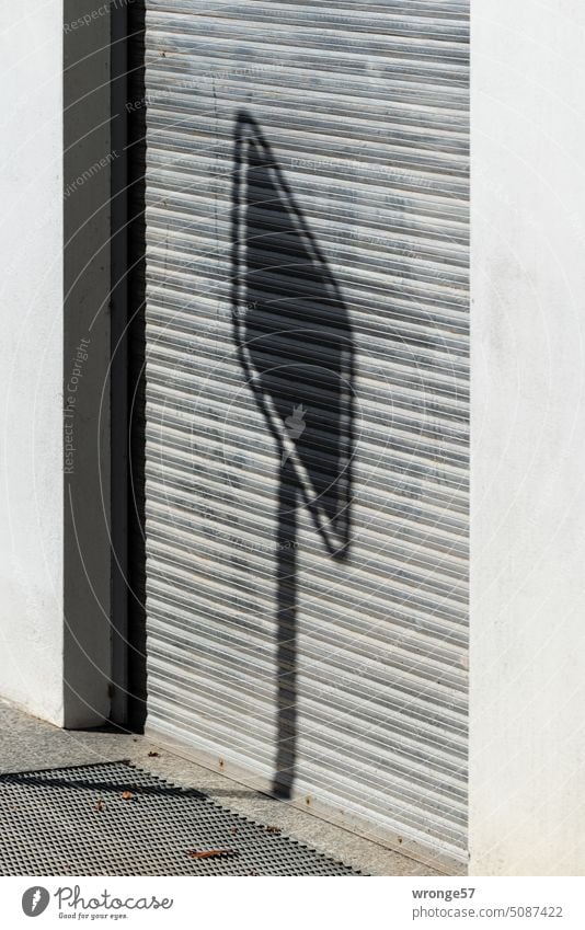 Schatten eines Schildes fällt auf die geschlossene Jalousie eines Rolltores Eingang Tür Gebäude Tor Sonnenschein Außenaufnahme Menschenleer