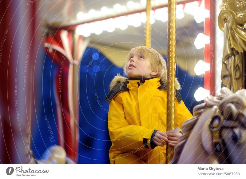 Niedlicher blonder Junge auf dem Weihnachtsmarkt. Kleines Kind reitet auf einem Oldtimer-Karussell (Merry Go Round). Draußen Unterhaltung Aktivität für Kinder in den Winterferien