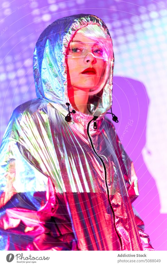 Frau in silberner Jacke schaut in die Kamera Model neonfarbig leuchten futuristisch Zeitgenosse Studioaufnahme glühen emotionslos durchsichtig Schutzbrille
