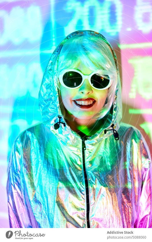 Futuristische Frau mit Sonnenbrille steht in einem Studio mit Projektorlicht Model Cyberpunk Nummer leuchten neonfarbig modern Zukunft Studioaufnahme Lächeln