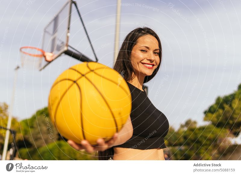 Lächelnde Frau mit orangefarbenem Ball auf dem Spielfeld Spieler Streetball zeigen Reifen Hobby Sport Aktivität heiter sportlich Sportlerin Energie Gericht
