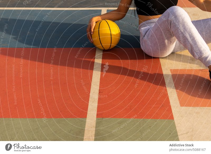 Anonyme Frau mit Basketball auf dem Boden sitzend beim Basketballtraining Ball anonym Ernte Gericht Pause sich[Akk] entspannen Streetball Hobby Training