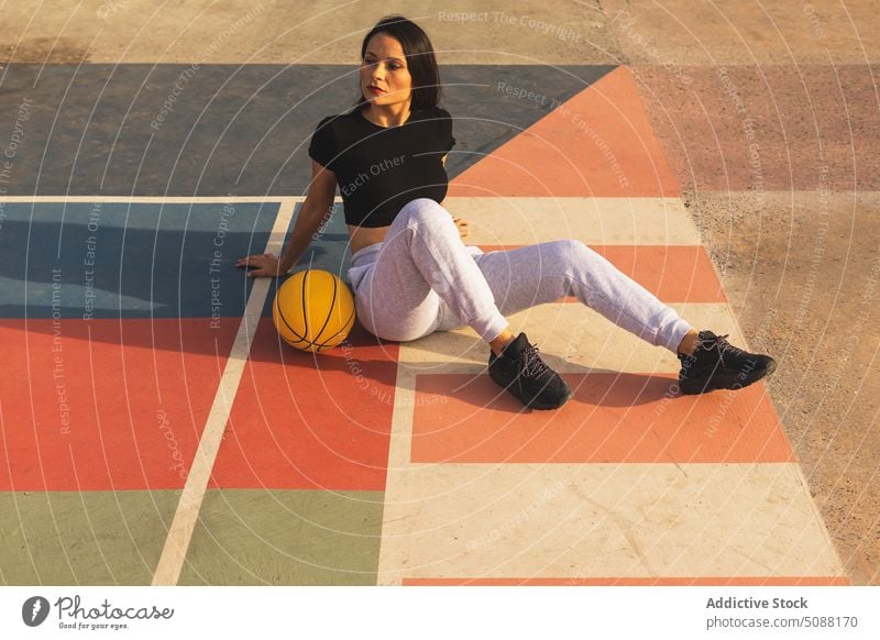 Fitte Frau mit Basketball auf dem Boden sitzend beim Basketballtraining Pause sich zurücklehnen Gericht sich[Akk] entspannen Ball Streetball Hobby Training