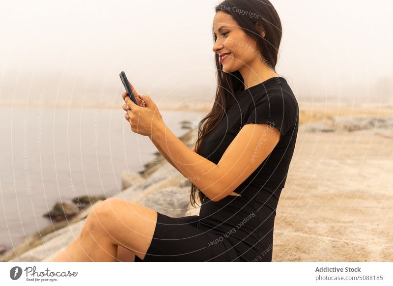 Sportlerin benutzt Smartphone in Meeresnähe bei Nebel Frau Selfie benutzend Pause soziale Netzwerke Training ruhen MEER sportlich positiv Lächeln passen Athlet