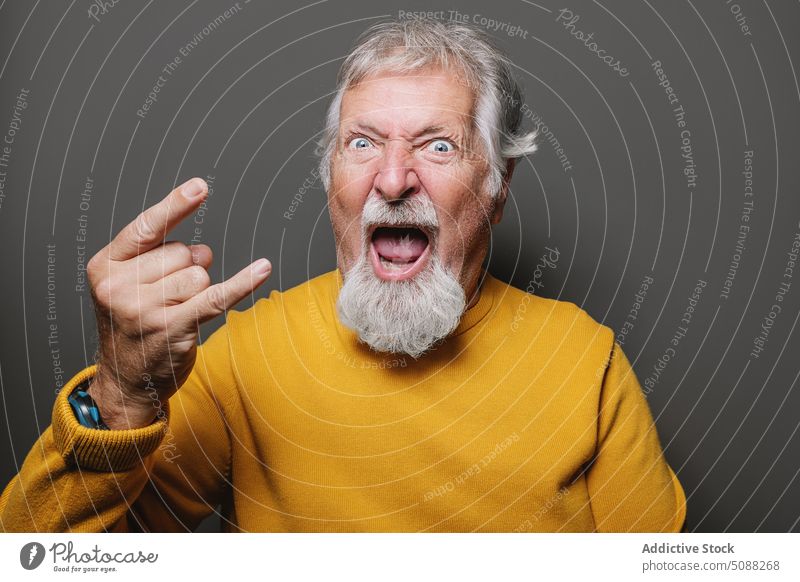 Älterer Mann zeigt Rock-Geste Porträt zeigen Felsen gestikulieren Hupe Zeichen Rock and Roll cool Senior älter gealtert männlich graues Haar Vollbart gelb