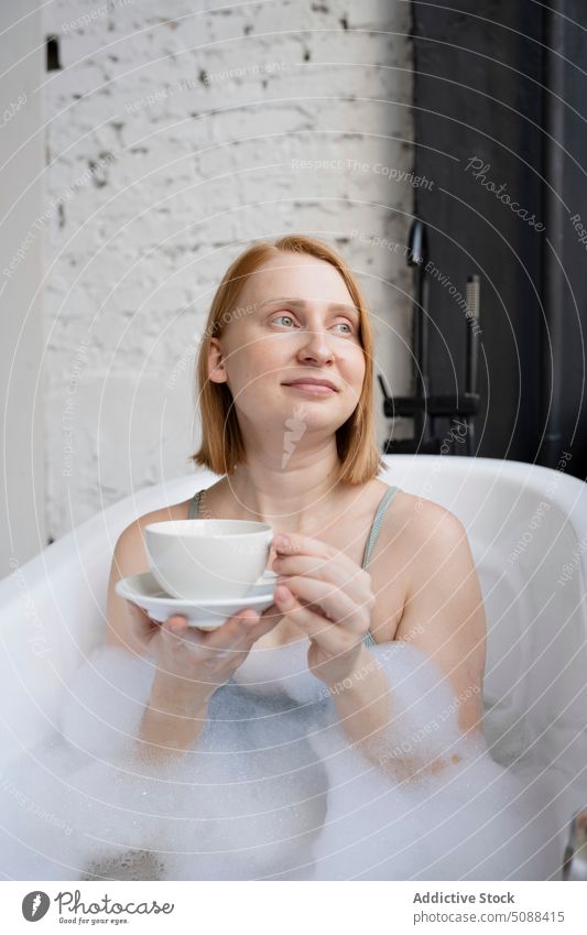 Frau in Badewanne mit Becher mit Getränk sich[Akk] entspannen schäumen Tasse Heißgetränk Untertasse Routine Hygiene verträumt Lächeln täglich Erfrischung