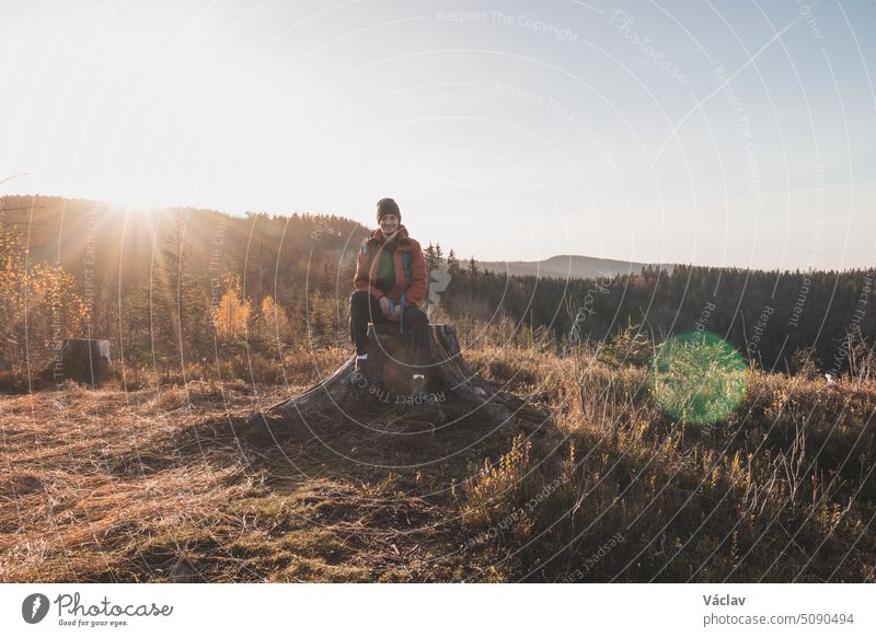 Ein aktiver Wanderer sitzt auf einem Baumstumpf und genießt das Gefühl, bei Sonnenaufgang den Gipfel des Berges zu erreichen. Ein Wanderer wird von der Morgensonne erleuchtet und genießt die Aussicht. Beskiden, Tschechische Republik