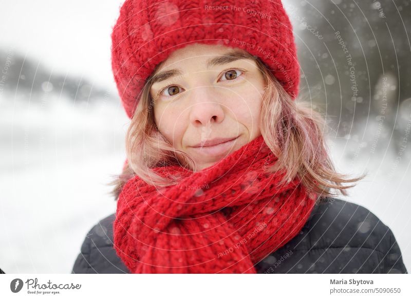 Close-up-Porträt der jungen schönen kaukasischen Frau mit rosa Haaren trägt rote Mütze und Schal bei Schneefall am Wintertag. niedlich Kleidung Hut Behaarung