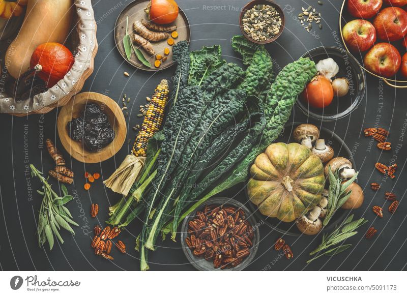 Gesunde, saisonale, vegane Zutaten: Grünkohl, Kürbis, Mais, Äpfel, Pekannüsse und Samen mit frischen Kräutern und Gewürzen auf einem rustikalen Küchentisch, Ansicht von oben