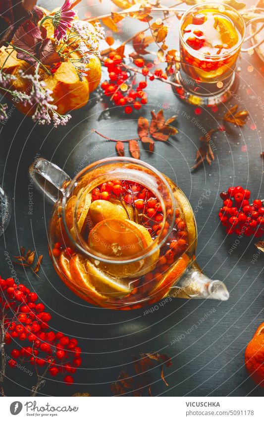 Klasse Teekanne mit gesundem Vitamintee mit Vogelbeeren, Orangen- und Zitronenscheiben auf einem Tisch mit Zutaten. Heißes Getränk für die kalte Herbstzeit. Nahaufnahme