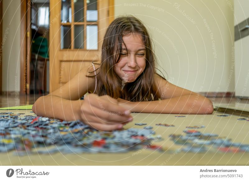 Ein brünettes Teenager-Mädchen, das auf dem Boden ihres Hauses ein Puzzle macht. Sie verbringt ihre Zeit damit, der Technologie zu entfliehen und traditionelle Spiele zu genießen.