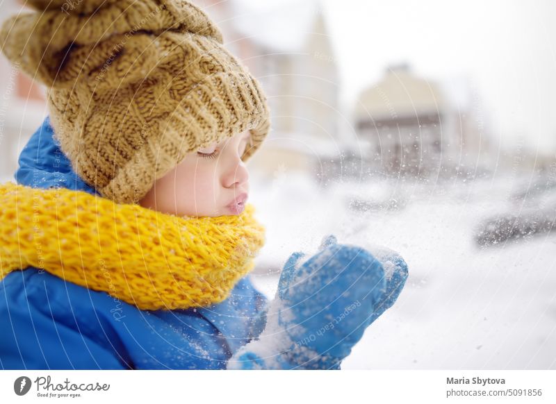 Kleiner Junge bläst Schnee aus seinen Händen. Kind genießen Spaziergang im Park auf verschneiten Tag. Baby mit Spaß während Schneefall. Outdoor-Winter-Aktivitäten für Kinder.
