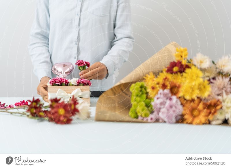 Crop-Frau arrangiert Blumen in einer Schachtel Blumenhändler einrichten Nelke Blumenstrauß Kasten Schleife präsentieren kreativ geblümt Floristik