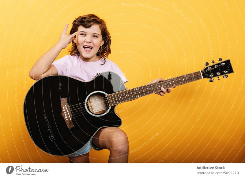 Fröhliches Mädchen mit Gitarre und Rock-Geste zeigen Felsen gestikulieren Hupe Zeichen Rock and Roll spielen akustisch Glück aufgeregt heiter Kind unterhalten