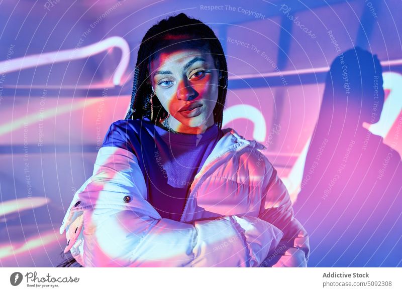 Trendige afroamerikanische Frau schaut in die Kamera in einem beleuchteten Studio selbstbewusst Stil selbstsicher glühen neonfarbig Model traumhaft