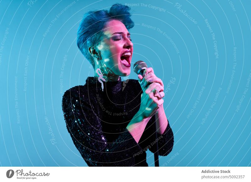 Junge Frau mit Mikrofon singt im Studio singen Gesang Hipster Licht neonfarbig Atelier Sänger Aufzeichnen positiv leuchten Musiker jung Klang ausführen blau