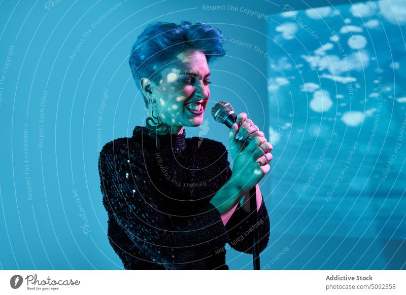 Junge Frau mit Mikrofon singt im Studio singen Gesang Hipster Licht neonfarbig Atelier Sänger Aufzeichnen positiv leuchten Musiker jung Klang ausführen blau
