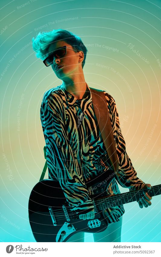 Stilvolle Frau spielt Gitarre in buntem Studio elektrisch spielen Musik Musiker Gitarrenspieler trendy Hipster Mode Outfit Sonnenbrille Instrument Melodie Klang