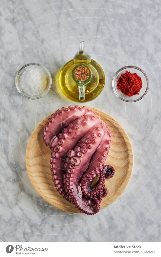 Oktopus auf Holzteller mit Gewürzen und Öl Octopus mediterran Tentakel ungekocht Speise Erdöl Lebensmittel Küche Paprika rund hölzern Teller Meeresfrüchte