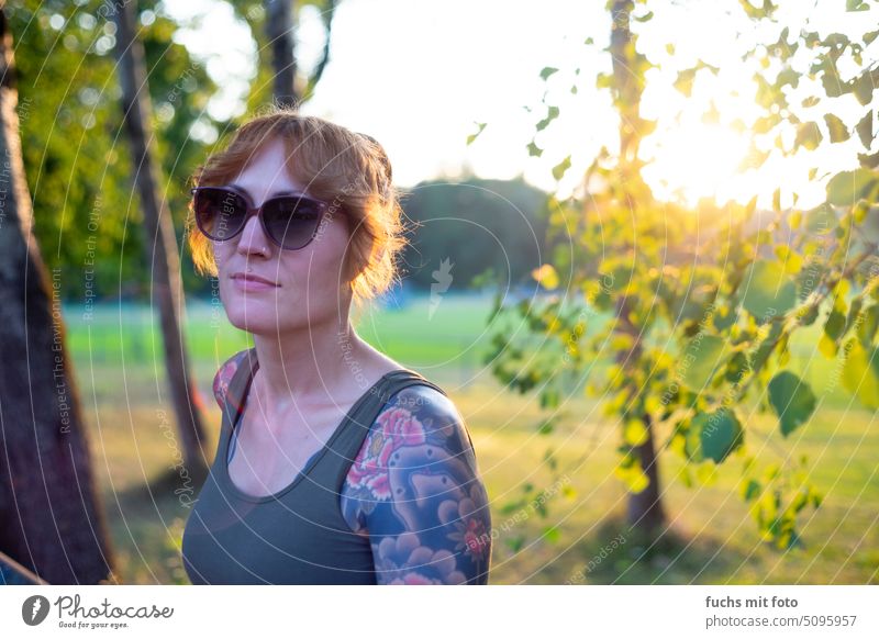 Frau mit Sonnenbrille und Tattoo im Sonnenuntergang Tätowierung tätowiert sonnenbrille gegenlicht vintagelens bokeh lensflair natur blätter sommer Mensch