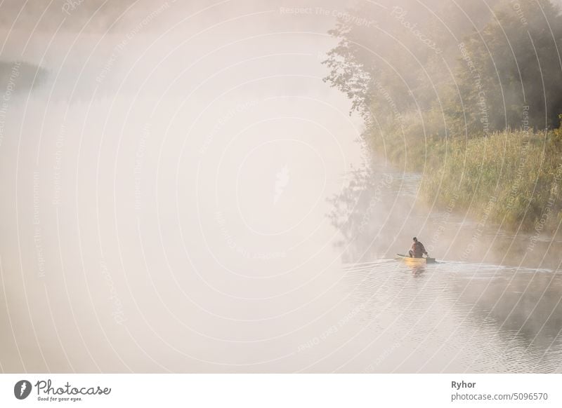 Calm Lake, River And Man Fishing From Old Wooden Rowing Fishing Boat At Beautiful Misty Sunrise In Summer Morning. Fischer ist in hölzernen Boot. Russische Natur. Ökotourismus