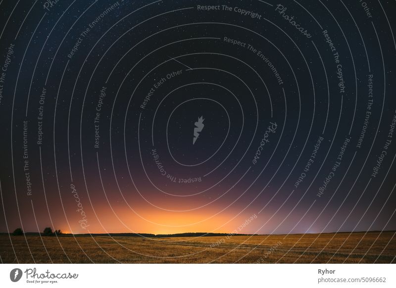 Natural Night Starry Sky Above Field Meadow. Glühende Sterne, Meteoriten Spur und Sonnenuntergang Sonnenaufgang Lichter über Landschaft im August Monat. Meteoric Track In Nachthimmel Hintergrund