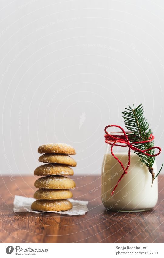 Ein Glas Milch mit Tannenzweig und roter Schleife und gestapelte Kekse auf einem Holztisch. Weihnachten. Weihnachten & Advent gebacken süß lecker Dessert