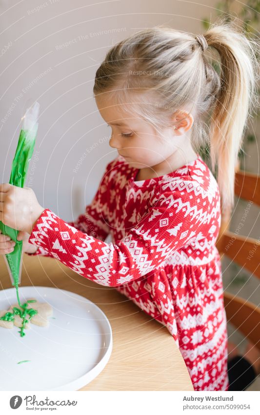 Kleines Mädchen, das einen Weihnachtskeks mit grünem Zuckerguss verziert backen Schönheit Feier Kind Kindheit Kinder Weihnachten Weihnachtsbaum Nahaufnahme Keks