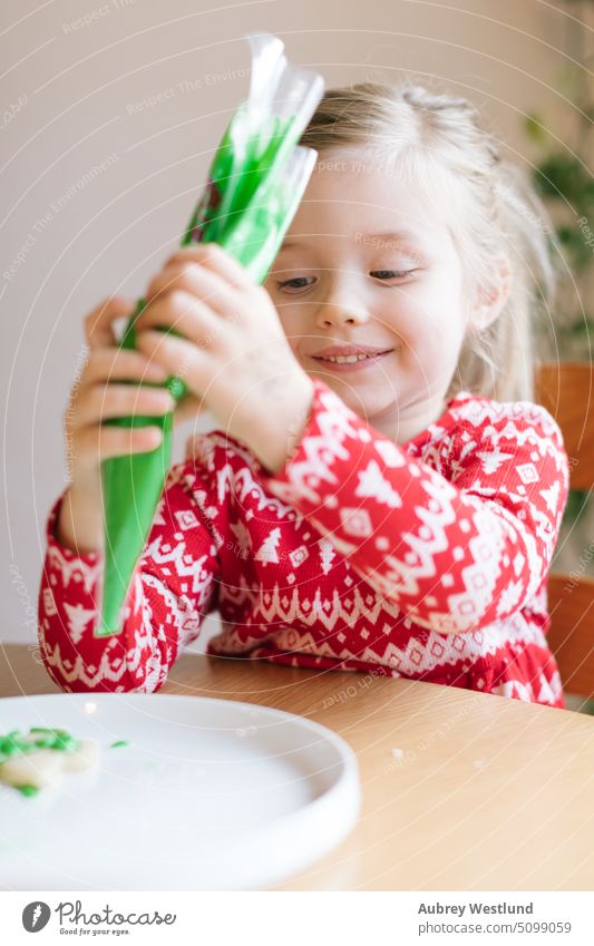 glückliches kleines Mädchen, das einen Weihnachtskeks mit grünem Zuckerguss verziert Weihnachten rot Feiertag Geschenk Kind Winter weiß Glück niedlich Porträt