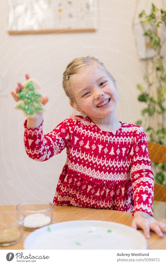 Lächelndes kleines Mädchen im roten Weihnachtspulli zeigt ihren Weihnachtsbaumkeks backen Schönheit Feier Kind Kindheit Kinder Weihnachten Nahaufnahme Keks