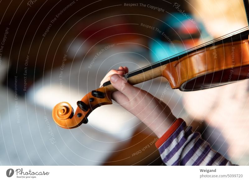 Detailaufnahme einer Kinderhand im Vordergrund, die eine Geige hält und spielt, während im Hintergrund verschwommen ein Notenbuch zu erahnen ist Musik