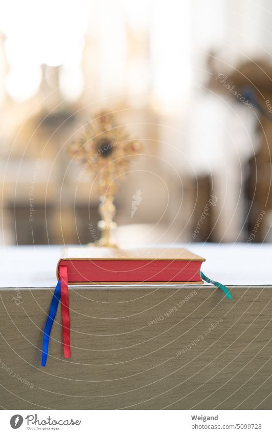 Detailaufnahme Bibel oder Gesangbuch mit rotem Schnitt und bunten Lesebändchen auf einem Altar vor einem verschwommenen Kreuz im Hintergrund bei Lichteinfall