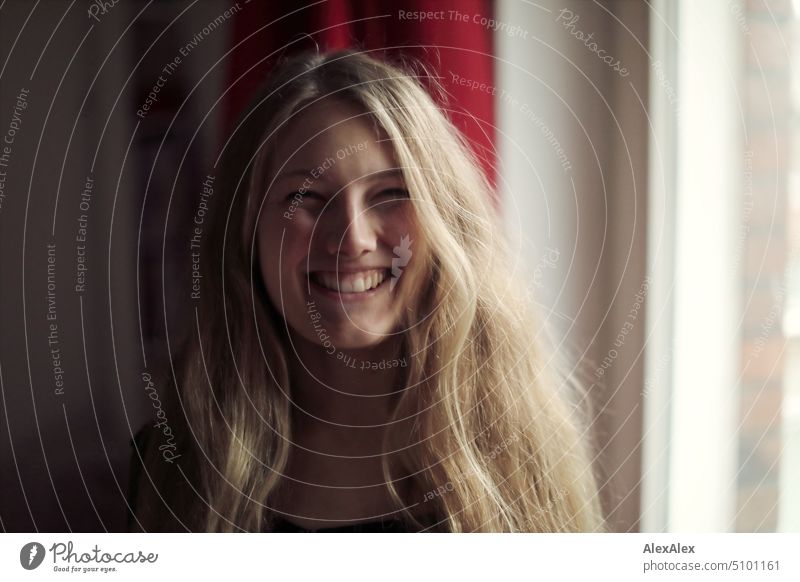 Nahes Portrait einer jungen, blonden Frau, die lächelnd am Fenster steht junge Frau langhaarig Freude schlank freundlich angenehm schön Porträt attraktiv