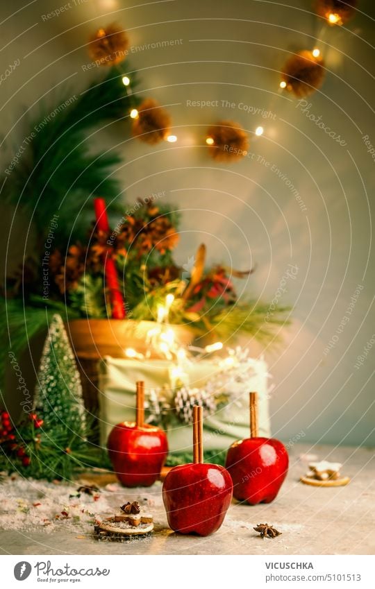 Rote Weihnachtsäpfel mit Zimtstangen auf einem Tisch mit Weihnachtsbaum, Geschenkbox und Bokeh. Vorderansicht Weihnachten rot Äpfel Geschenkverpackung festlich