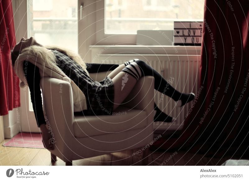 Portrait einer jungen blonden Frau, die schräg in einem Sessel liegt und lacht junge Frau Balkon Balkontür Beine Kniestrümpfe Kleid lächeln Freude Gelassenheit